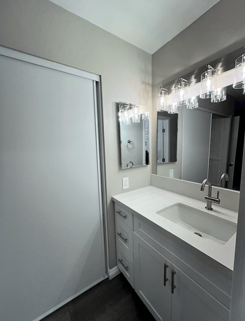 A bathroom with a sink, mirror, and lighting fixture.